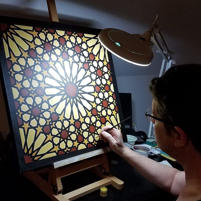 Photograph of Andrew working on a painting depicting an Islamic geometric pattern.
